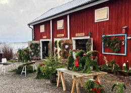 Ett rött verkstadshus i Rasmusbyn med julbockar gjorda av granris framför byggnaden, en vinterbild inför julmarknaden nära Örebro.